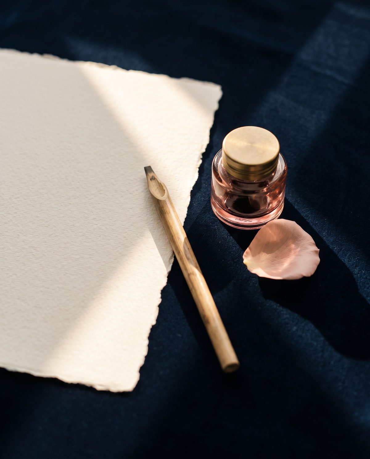 Handmade cream paper, a reed pen and a rose ink pot on navy velvet in a beam of sunlight